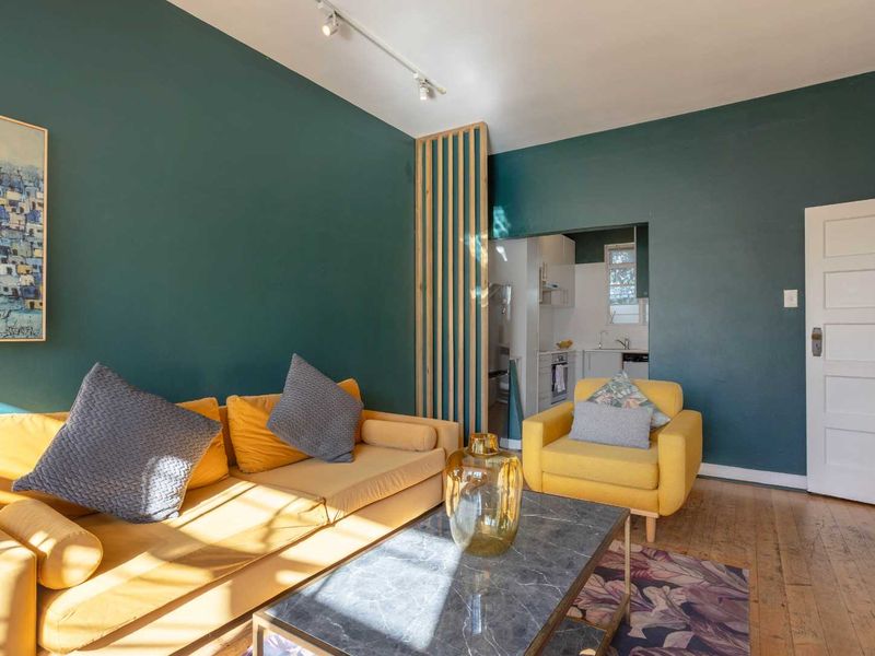 Open plan living area featuring dark teal walls, hardwood flooring, a decorative timber slat room divider, and track lighting, with an adjacent kitchen view.