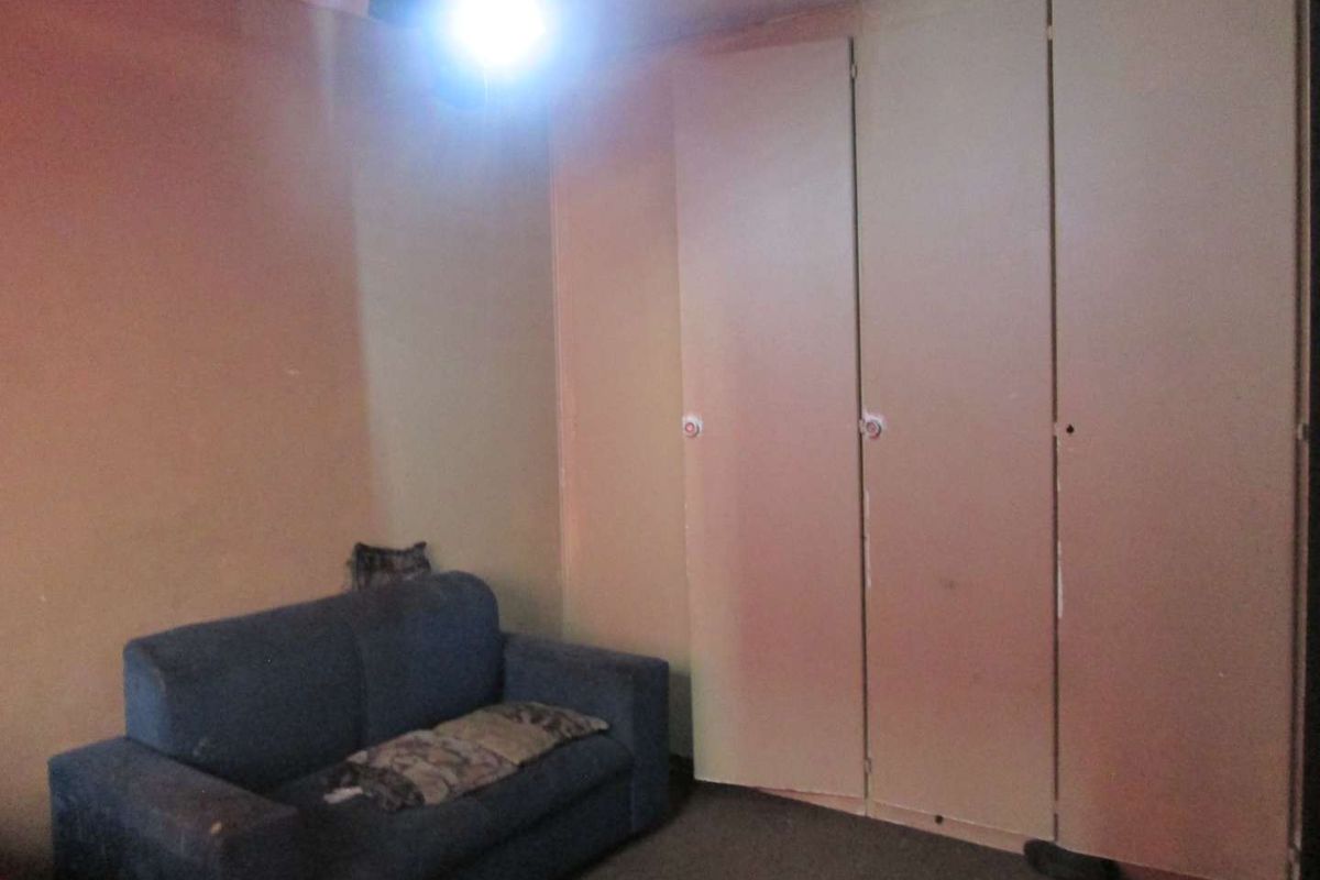 A bedroom featuring built-in cupboards with a dated finish and worn wall and floor surfaces.