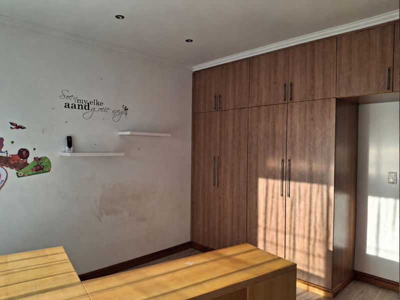 A bedroom featuring extensive built-in wooden cupboards, recessed downlighting, and laminate flooring, offering ample storage space.
