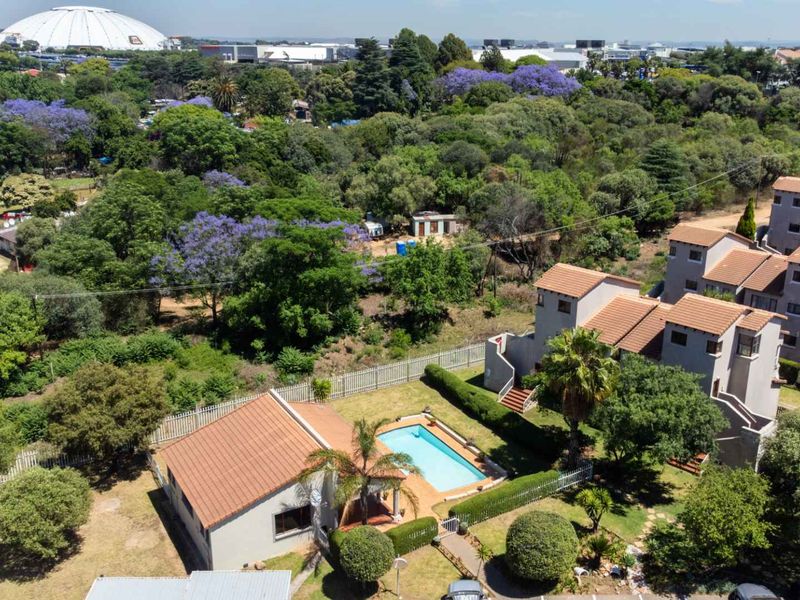 Aerial view of the apartment complex featuring a swimming pool, landscaped gardens, and tiled roof structures within a suburban setting.