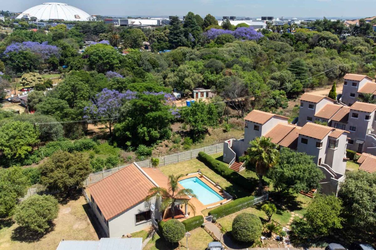 Aerial view of the apartment complex featuring a swimming pool, landscaped gardens, and tiled roof structures within a suburban setting.