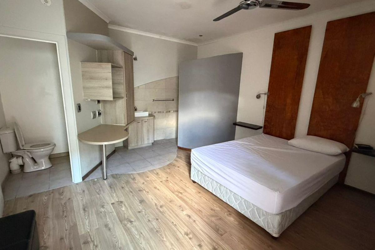 A bedroom featuring wood-look laminate flooring, built-in cabinetry, and an open-plan en-suite bathroom with a toilet and vanity.