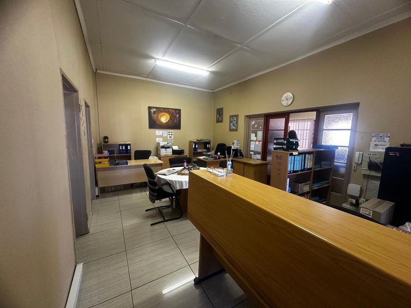 A functional office space featuring tiled flooring, fluorescent lighting, and a built-in reception counter, suitable for professional use.