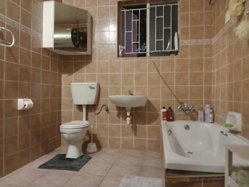 A dated bathroom featuring ceramic wall and floor tiles, a wall-mounted basin, a standard toilet, and a bathtub with exposed plumbing fixtures.