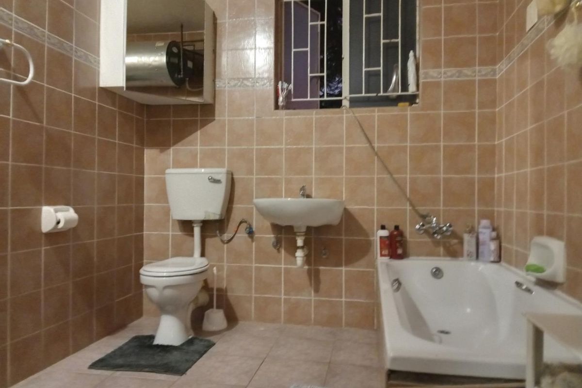 A dated bathroom featuring ceramic wall and floor tiles, a wall-mounted basin, a standard toilet, and a bathtub with exposed plumbing fixtures.