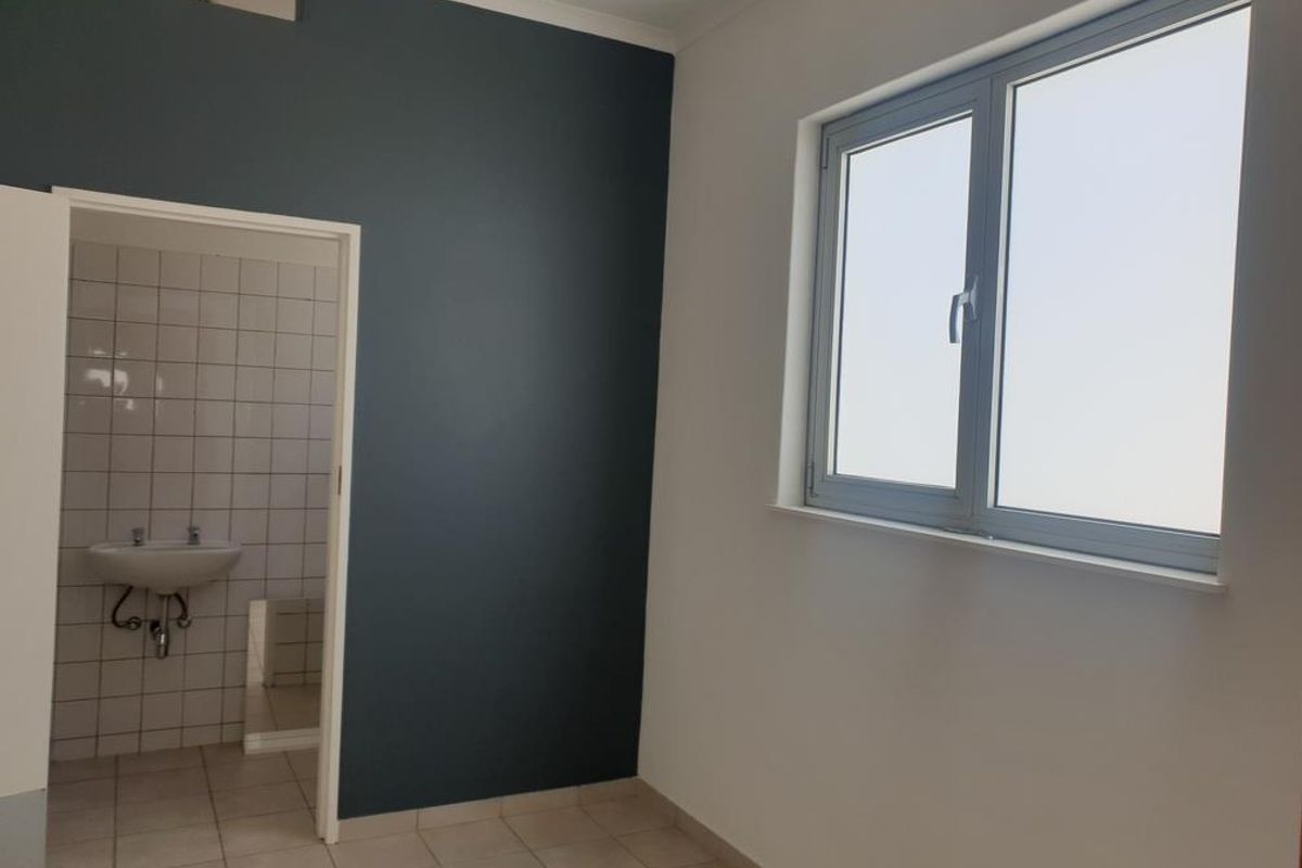 A clean, empty room featuring a dark accent wall, tiled flooring, and a view into an adjacent tiled bathroom with a wall-mounted basin.
