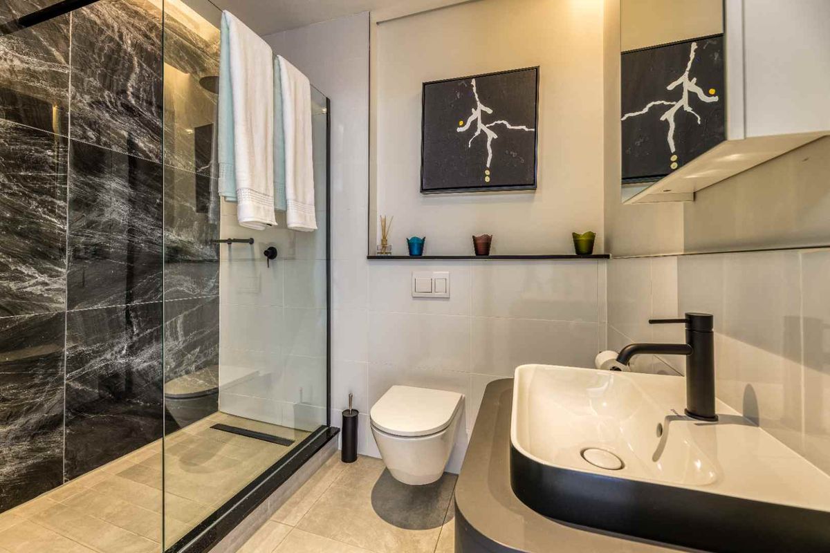Modern bathroom featuring a walk-in shower with dark marble-effect tiling, a wall-mounted toilet, and a contemporary vanity basin with matte black fixtures.