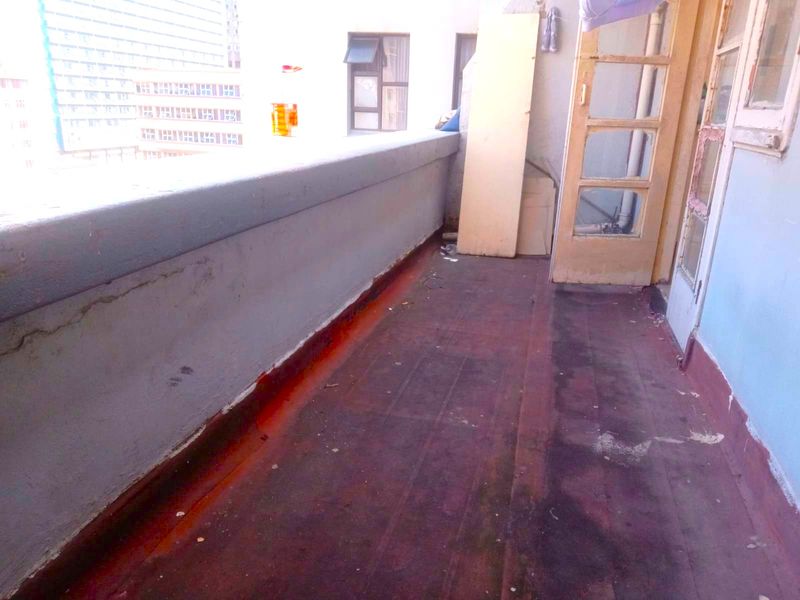 An outdoor balcony area featuring a concrete balustrade and access via a timber-framed glass door, currently showing signs of significant wear and weathering.