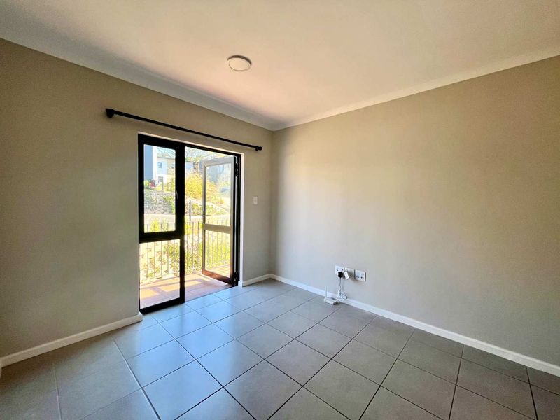 A bright, empty living area featuring neutral tiled flooring, cove cornicing, and a sliding glass door providing access to an outdoor balcony.