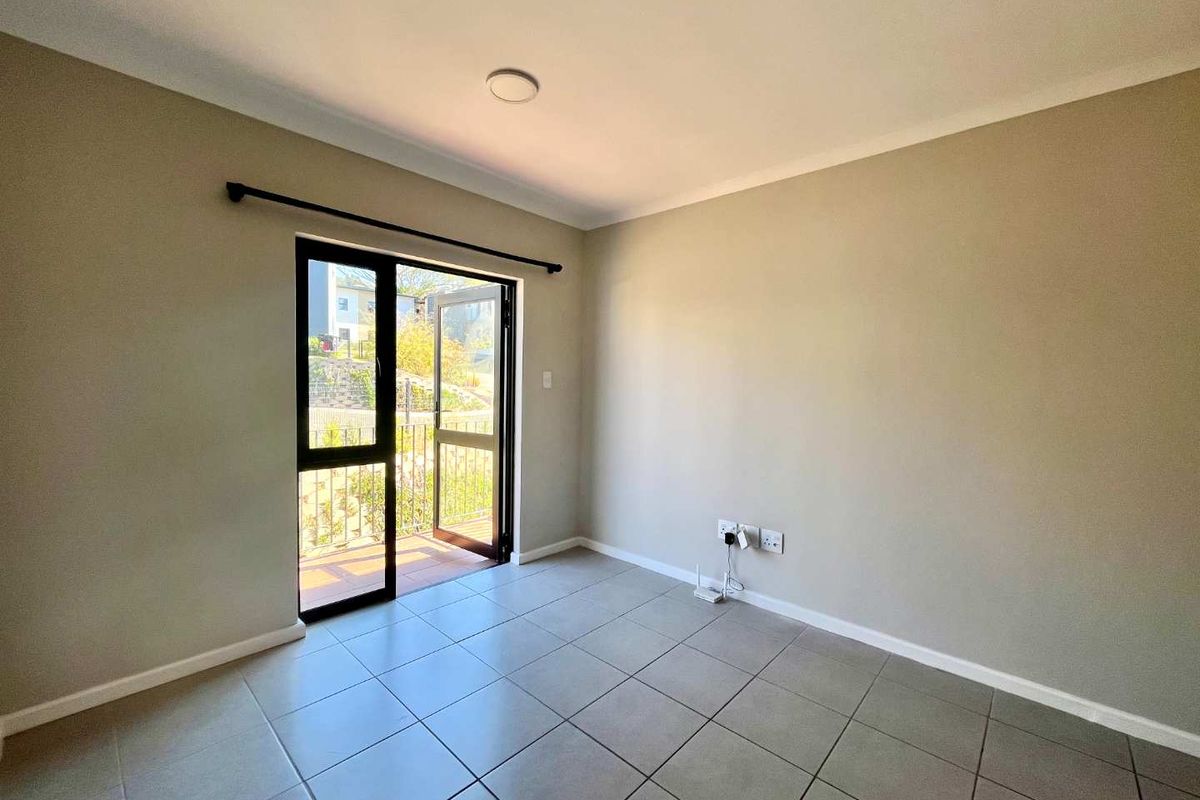 A bright, empty living area featuring neutral tiled flooring, cove cornicing, and a sliding glass door providing access to an outdoor balcony.