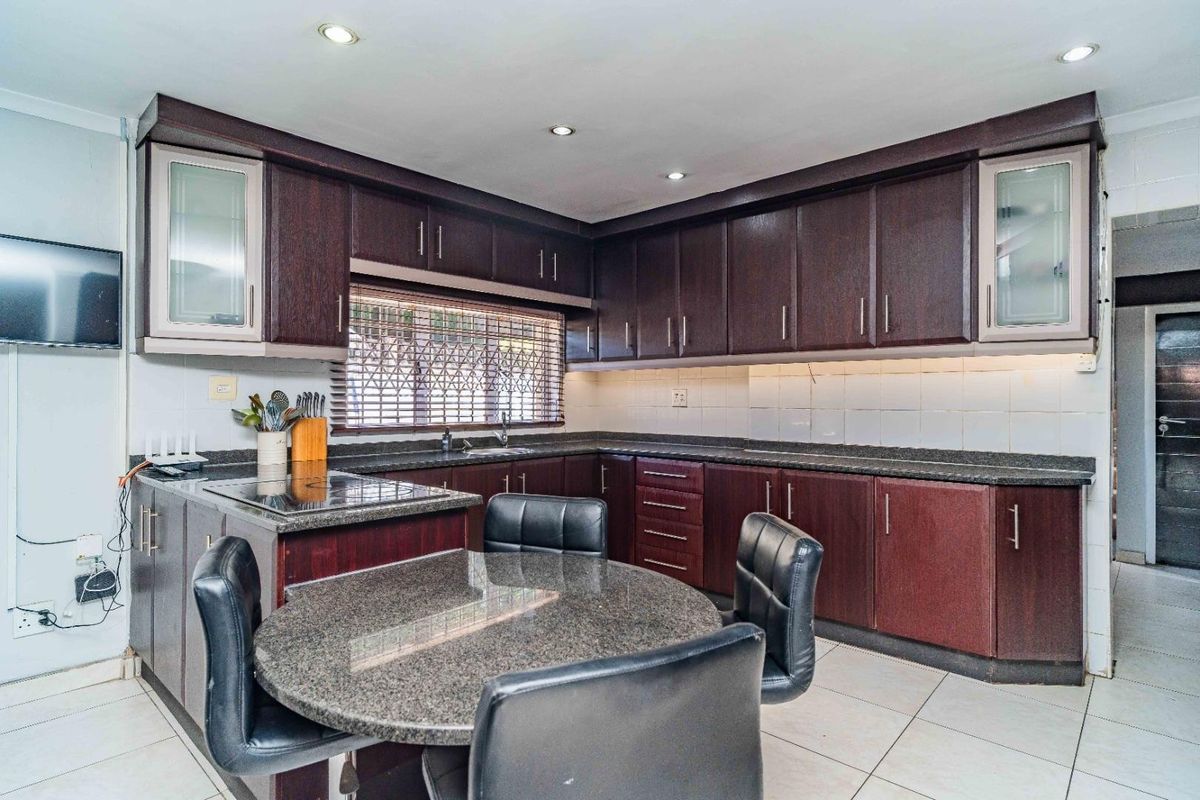 A functional kitchen featuring dark wood cabinetry, granite countertops, an integrated electric hob, and tiled flooring with recessed lighting.