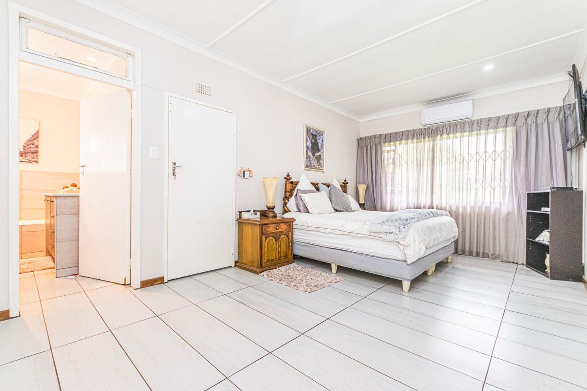 Spacious bedroom featuring large format floor tiles, an en-suite bathroom, and a wall-mounted air conditioning unit.