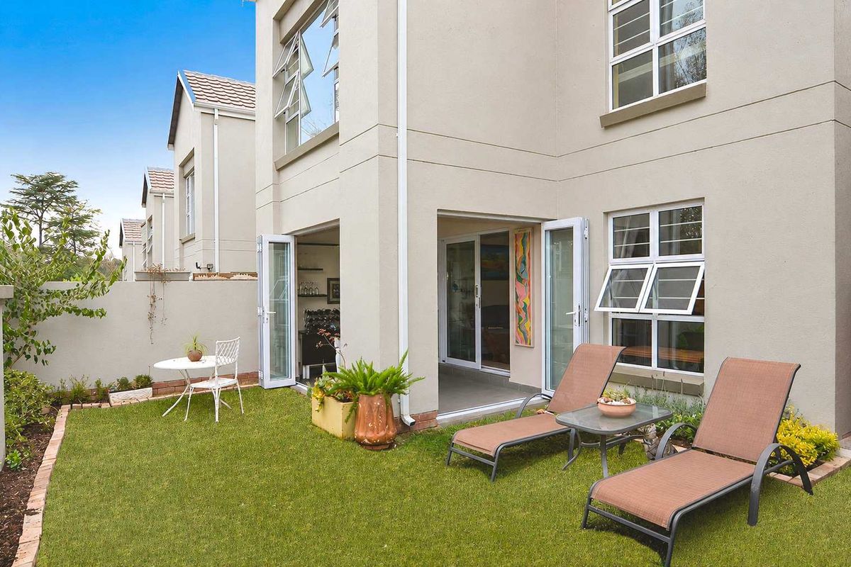 Rear view of the cluster home featuring a private garden, paved patio area, and seamless indoor-outdoor flow through bi-fold and sliding glass doors.