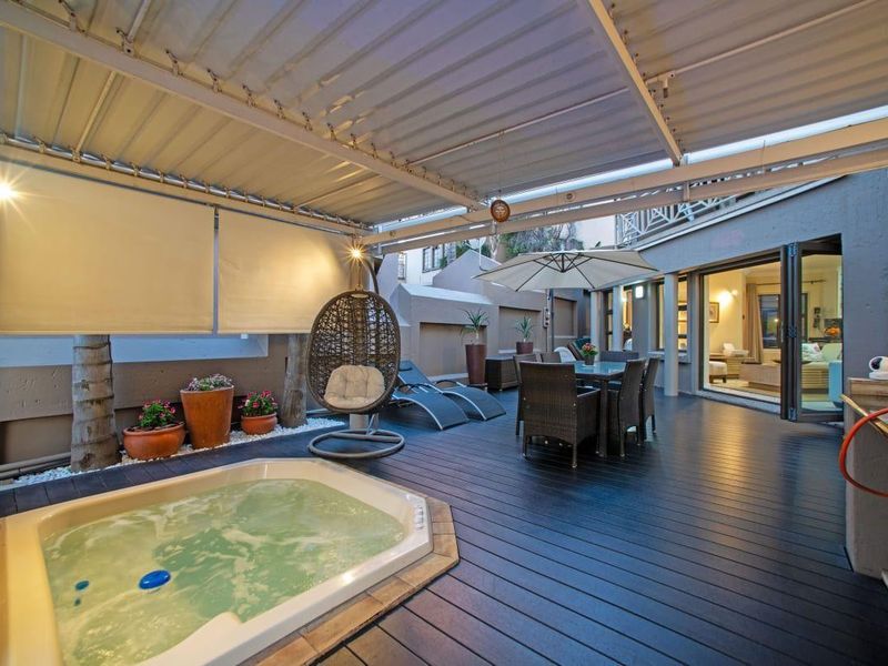 Covered outdoor patio featuring timber decking, a built-in jacuzzi, and seamless access to the interior living space through bi-fold doors.