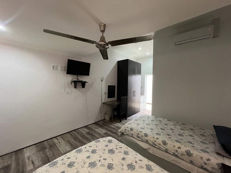 A functional bedroom featuring a ceiling fan, wall-mounted air conditioning unit, built-in wardrobe, and durable laminate flooring.