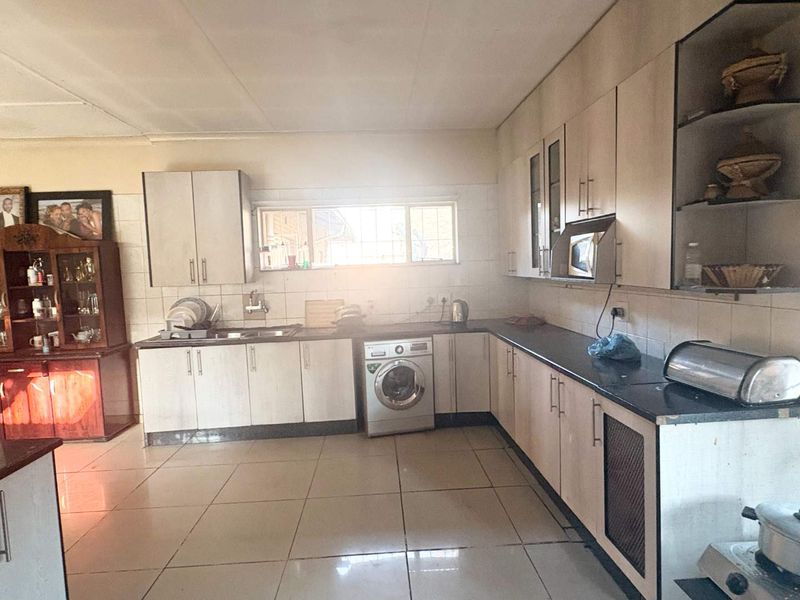 A functional kitchen featuring light-toned cabinetry, dark countertops, tiled flooring, and integrated laundry appliances, offering a practical layout for daily use.