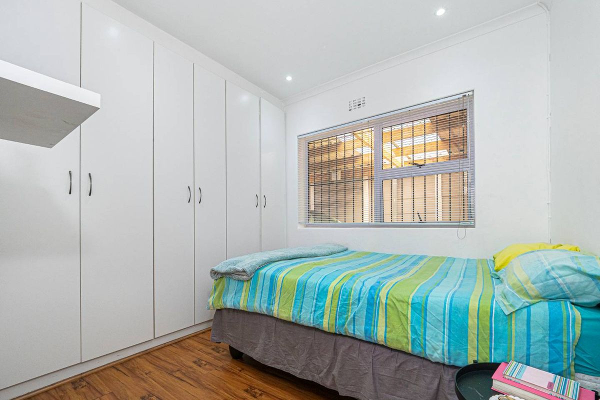 A bright bedroom featuring built-in floor-to-ceiling wardrobes, laminate timber flooring, and recessed downlighting.