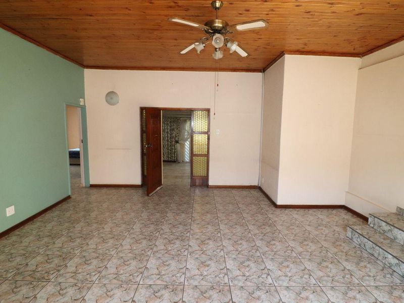 An empty living room featuring a timber-clad ceiling, ceiling fan, and ceramic tiled flooring with access to adjacent rooms via internal doors.
