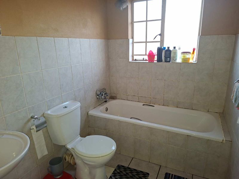 A functional bathroom featuring a standard bathtub, toilet, and washbasin with tiled finishes throughout.