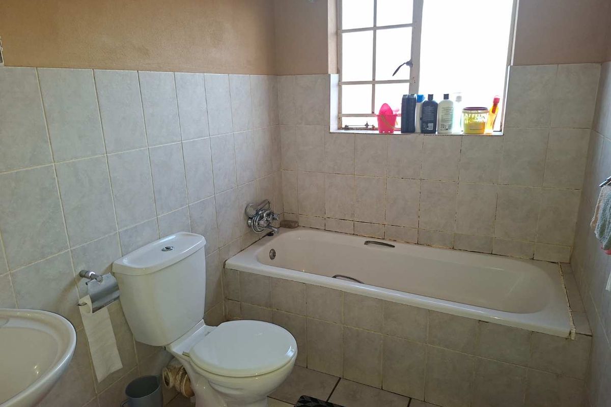 A functional bathroom featuring a standard bathtub, toilet, and washbasin with tiled finishes throughout.