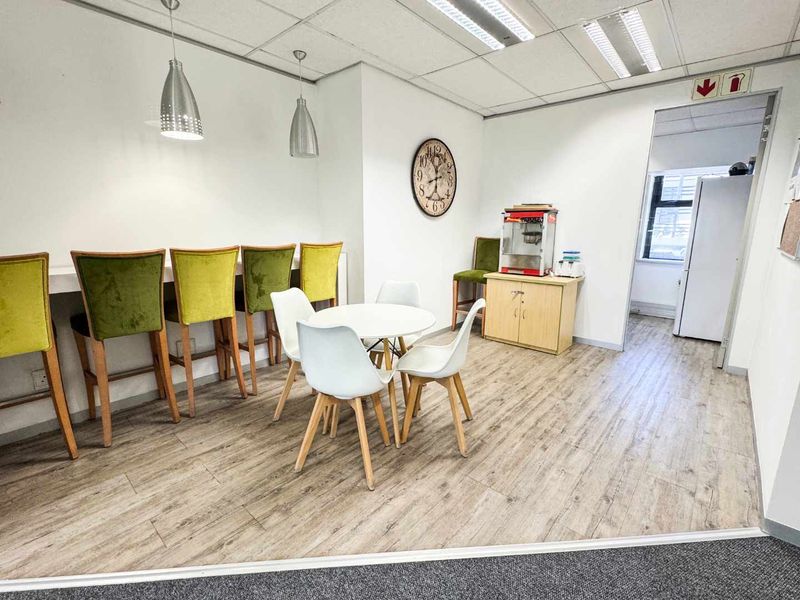 Open-plan office break area featuring laminate flooring, a built-in breakfast bar, and recessed ceiling lighting.