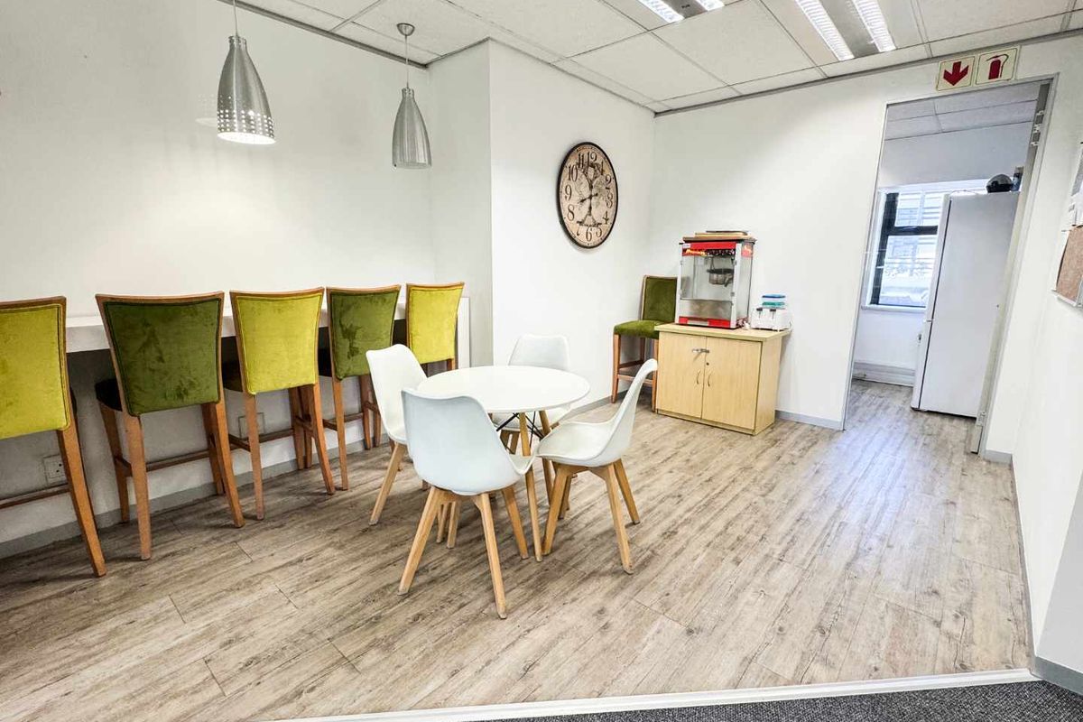 Open-plan office break area featuring laminate flooring, a built-in breakfast bar, and recessed ceiling lighting.