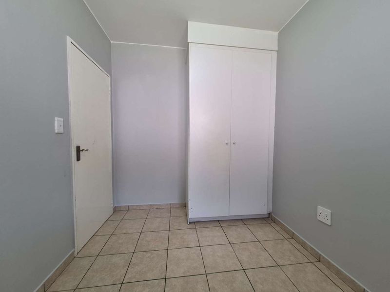An empty bedroom featuring neutral wall paint, tiled flooring, and a built-in wardrobe.