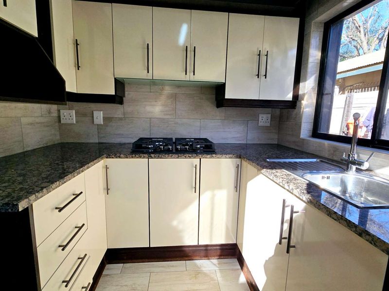 A modern, well-lit kitchen featuring granite countertops, ample built-in cabinetry, a gas hob, and a stainless steel sink with a window view.