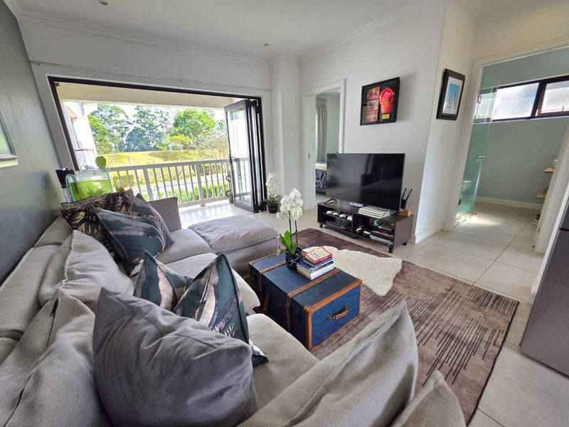 A bright living room featuring tiled floors and large bi-fold doors opening onto a balcony, with direct access to an adjacent bathroom.