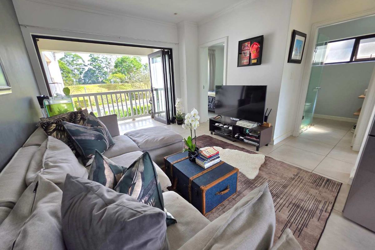 A bright living room featuring tiled floors and large bi-fold doors opening onto a balcony, with direct access to an adjacent bathroom.