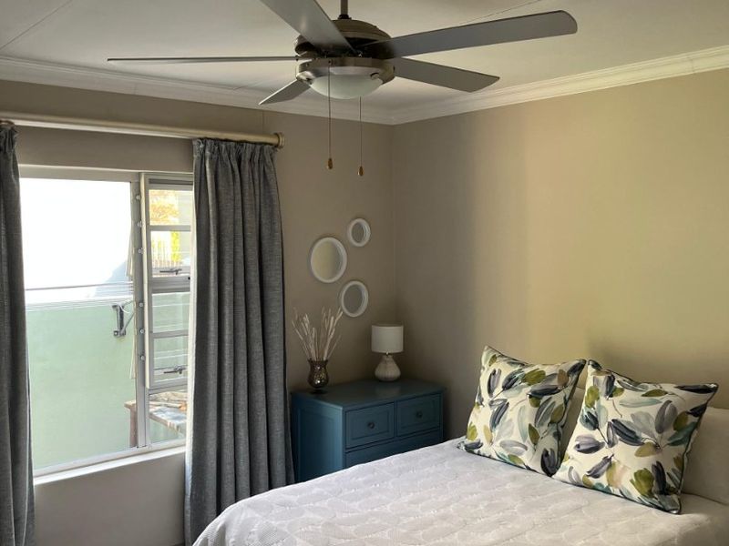 A well-maintained bedroom featuring laminate flooring, a ceiling fan, and a sliding window with neutral wall tones.