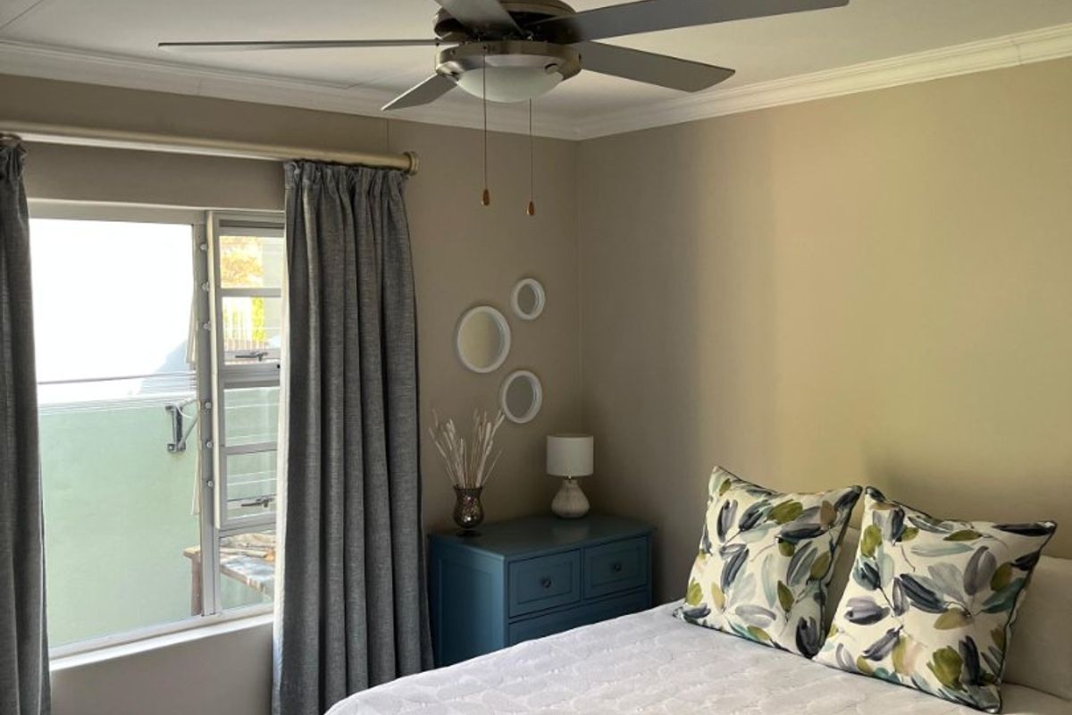 A well-maintained bedroom featuring laminate flooring, a ceiling fan, and a sliding window with neutral wall tones.