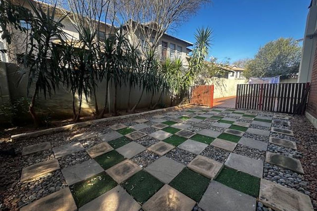 A low-maintenance rear garden area featuring a checkered pattern of paving stones and gravel, enclosed by boundary walls and a gated entrance.