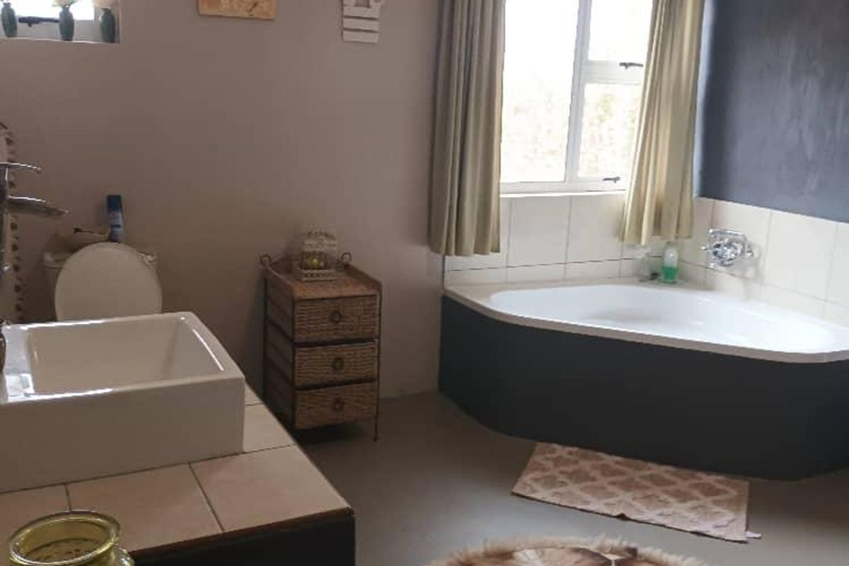 A functional bathroom featuring a corner bathtub, a tiled vanity with a basin, and a separate toilet area with natural light.