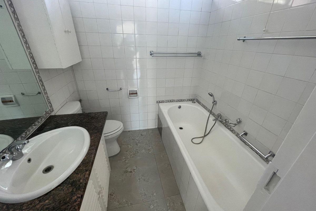 A functional bathroom featuring a bathtub, vanity with granite countertop, and white wall tiling. The space is clean and ready for potential modernization.