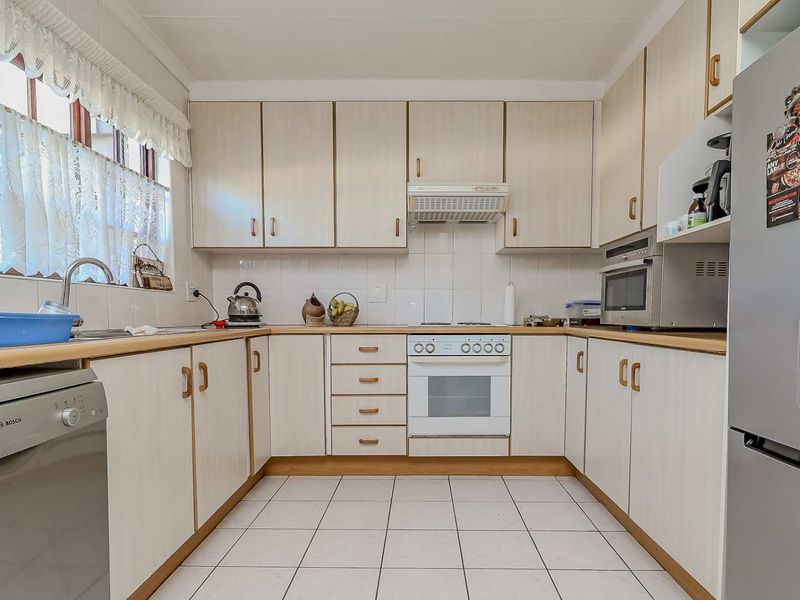 A functional kitchen featuring light-toned built-in cabinetry, laminate countertops, tiled backsplash, and integrated appliances including an oven, hob, and extractor fan.