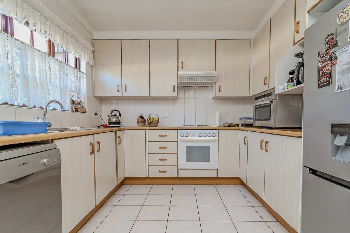 A functional kitchen featuring light-toned built-in cabinetry, laminate countertops, tiled backsplash, and integrated appliances including an oven, hob, and extractor fan.