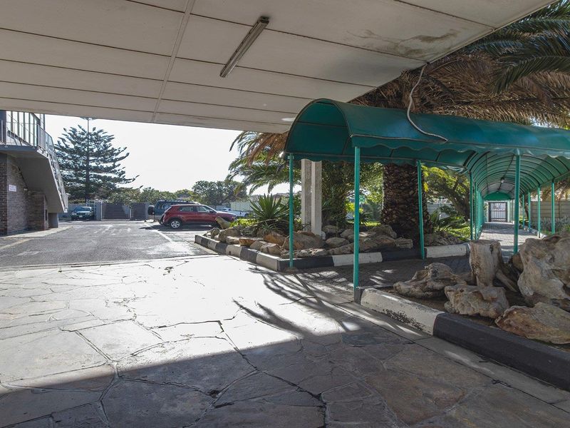A covered entrance area featuring a paved driveway, stone landscaping, and a sheltered walkway leading to the apartment building entrance.