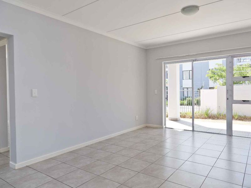 A bright, empty living room featuring neutral tiled flooring and a large sliding glass door providing access to the exterior.