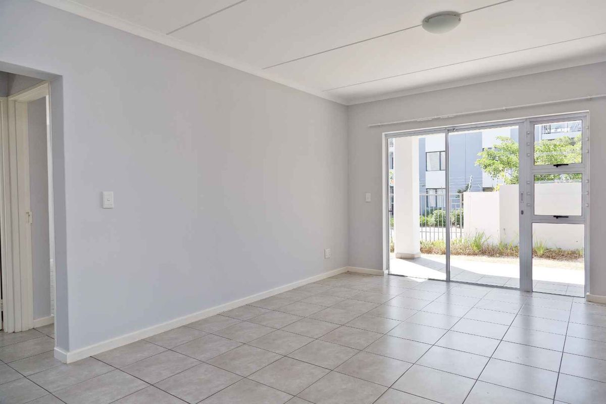 A bright, empty living room featuring neutral tiled flooring and a large sliding glass door providing access to the exterior.