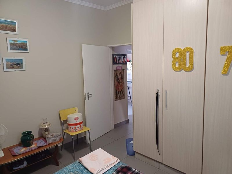 A bedroom featuring a large built-in wardrobe with light wood-grain finish and neutral tiled flooring.