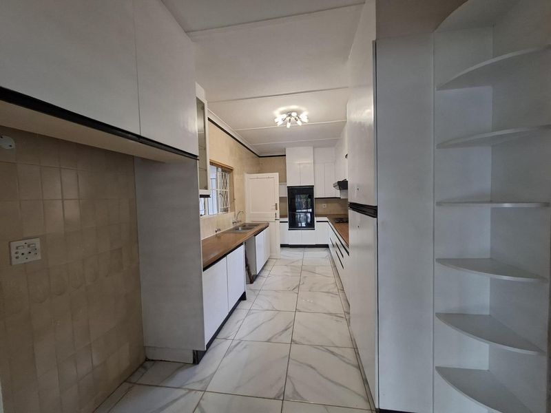 A clean, galley-style kitchen featuring white cabinetry, wooden countertops, built-in oven, and modern tiled flooring.