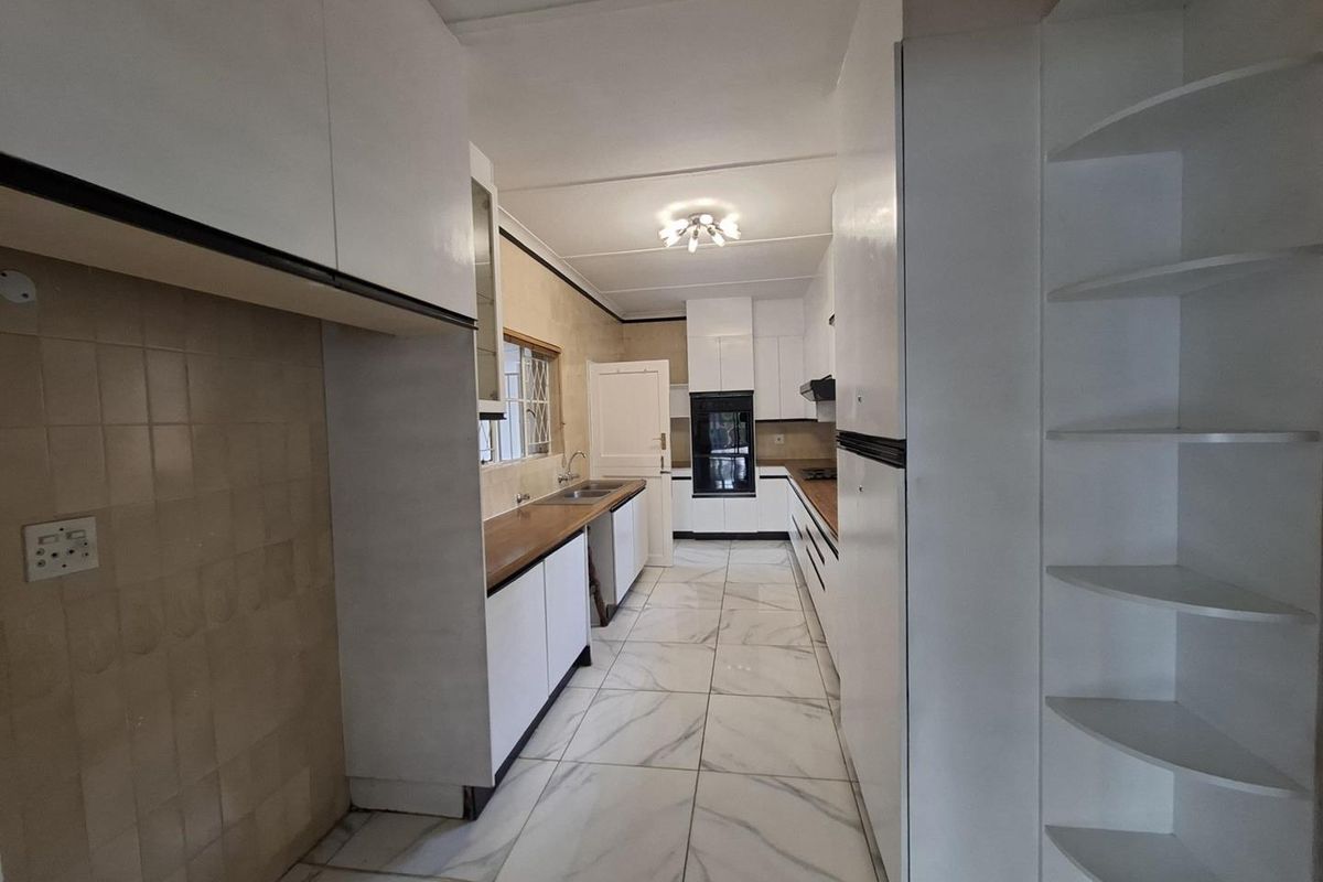 A clean, galley-style kitchen featuring white cabinetry, wooden countertops, built-in oven, and modern tiled flooring.
