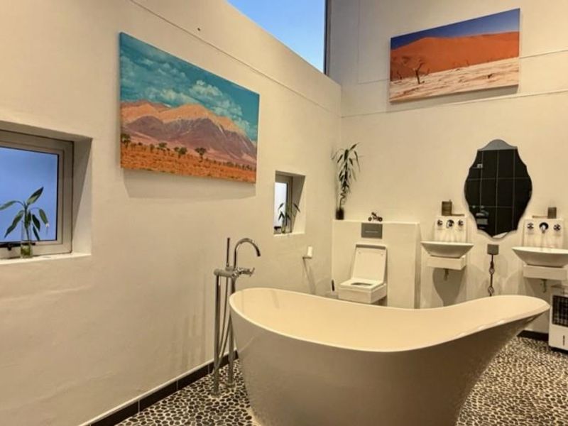Modern bathroom featuring a freestanding bathtub, dual wall-mounted basins, wall-hung toilet, and unique pebble flooring with high-level natural lighting.