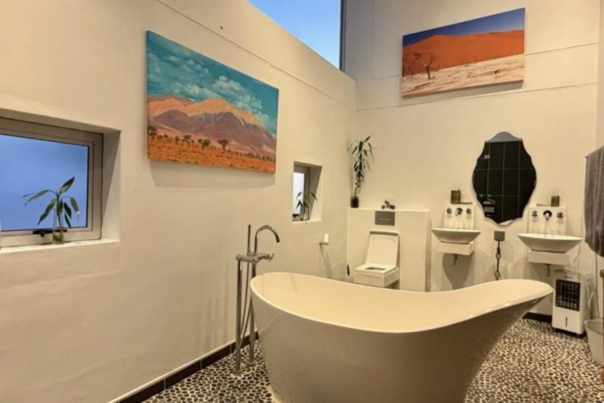 Modern bathroom featuring a freestanding bathtub, dual wall-mounted basins, wall-hung toilet, and unique pebble flooring with high-level natural lighting.