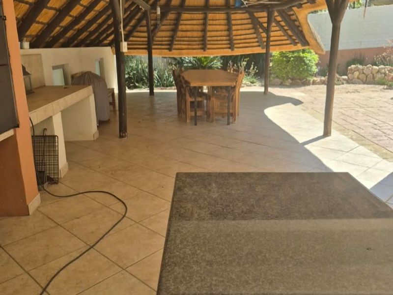Spacious covered patio featuring a traditional thatched roof, built-in braai area, and tiled flooring, perfect for outdoor entertaining.