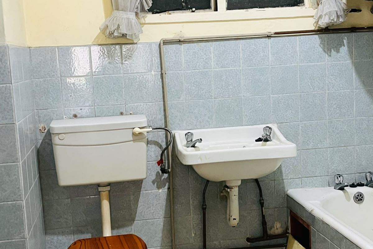 A dated bathroom featuring a wall-mounted basin, toilet cistern, and bathtub with exposed plumbing and tiled wall finishes.