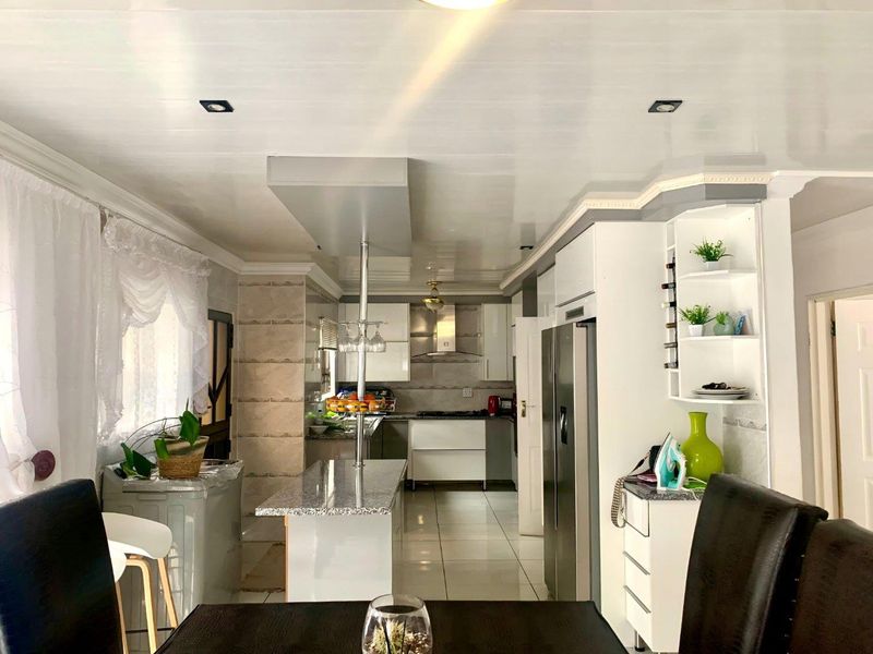 Modern open-plan kitchen featuring granite countertops, sleek cabinetry, a central island, and tiled flooring, creating a functional and bright cooking and dining space.