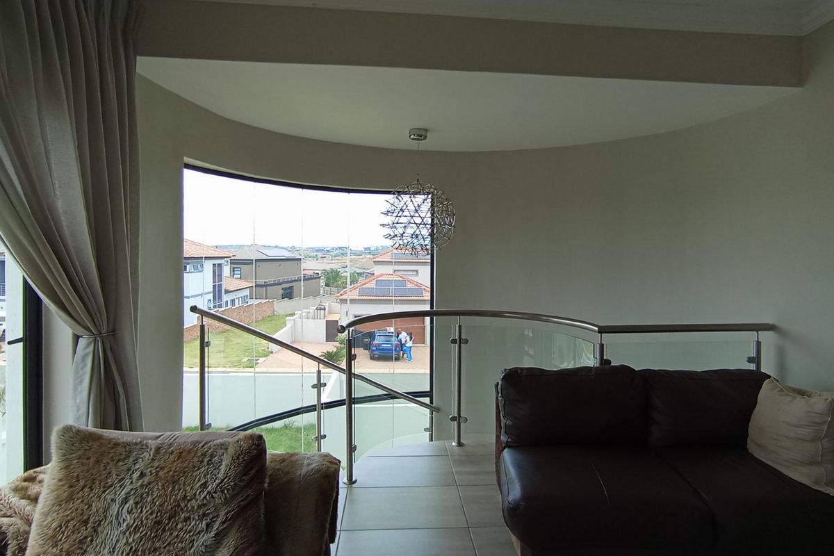 A bright living area featuring a curved glass balustrade overlooking the staircase and neighborhood views.