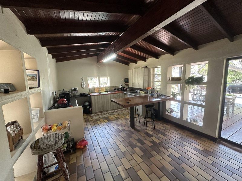 Spacious kitchen featuring exposed timber beam ceilings, tiled flooring, built-in cabinetry, and a central island, with large windows providing natural light and garden views.